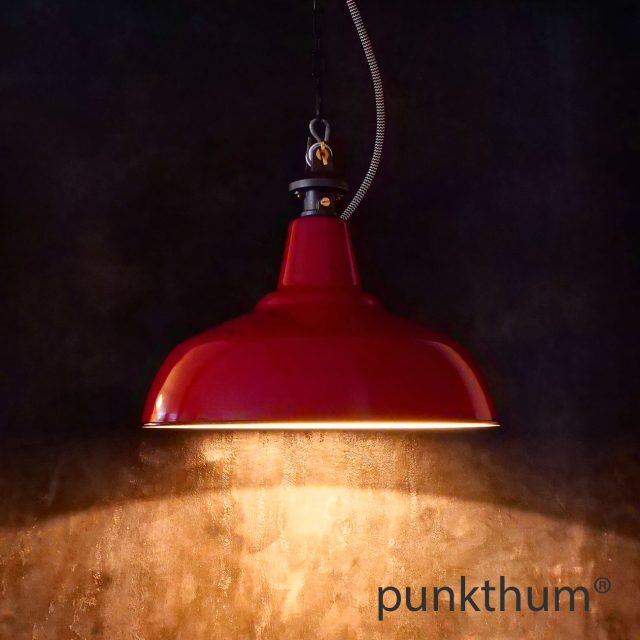 Rote Emaillelampe, Industrielampe mit Stahlguss-Aufhängung und Textilkabel, eingeschaltet.