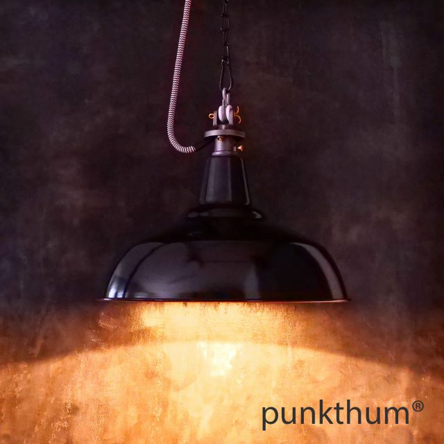 Schwarze Emaillelampe, Industrielampe mit Stahlguss-Aufhängung und Textilkabel, eingeschaltet.